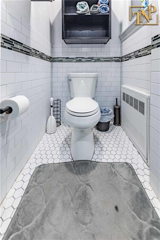bathroom featuring tile patterned flooring, radiator heating unit, toilet, and tile walls
