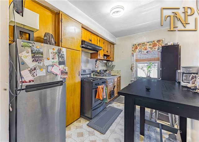 kitchen featuring black gas stove, freestanding refrigerator, under cabinet range hood, and brown cabinets