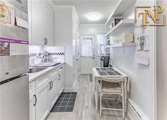 kitchen with light wood-type flooring, backsplash, crown molding, white cabinets, and stainless steel refrigerator