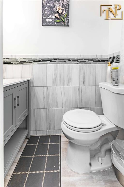 half bathroom with wainscoting, tile walls, vanity, and toilet