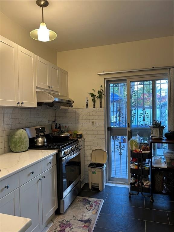 kitchen featuring light stone counters, backsplash, stainless steel gas stove, white cabinets, and dark tile patterned flooring