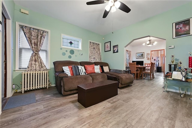 living room with light hardwood / wood-style floors, radiator, and ceiling fan with notable chandelier