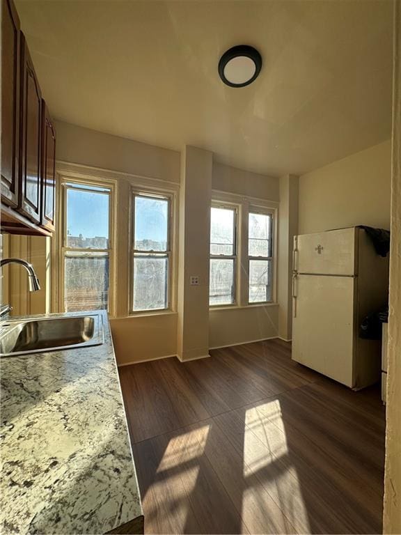 kitchen with white refrigerator, sink, dark wood-type flooring, and light stone counters