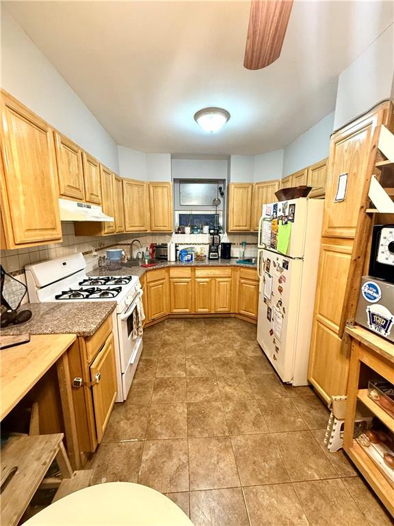 kitchen with white appliances, decorative backsplash, tile patterned flooring, under cabinet range hood, and a sink