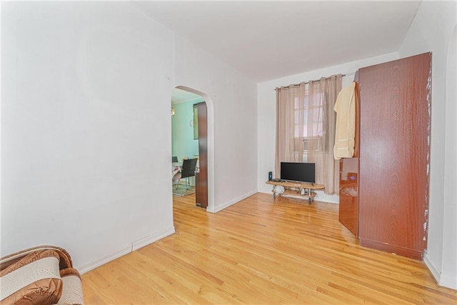 interior space with light wood-style floors, arched walkways, and baseboards