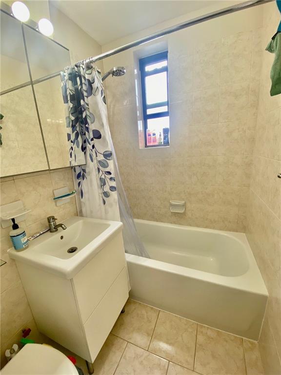 full bathroom with tile patterned floors, shower / bath combination with curtain, sink, toilet, and tile walls