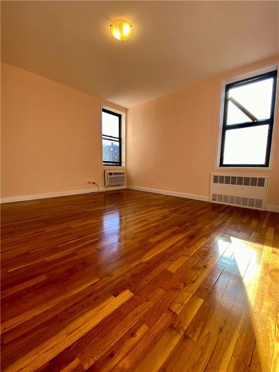 unfurnished room featuring a wall unit AC, radiator, and hardwood / wood-style floors