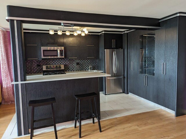 kitchen with pendant lighting, stainless steel appliances, light hardwood / wood-style floors, a kitchen bar, and beamed ceiling