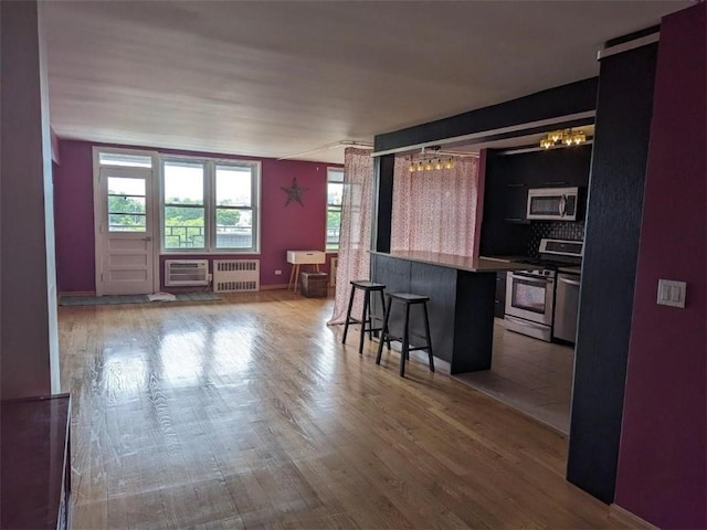 kitchen featuring a kitchen breakfast bar, stainless steel appliances, wood finished floors, and radiator