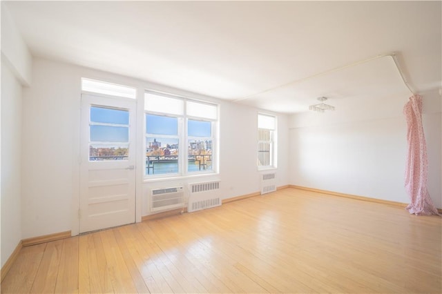 unfurnished room with radiator heating unit, wood-type flooring, baseboards, and an AC wall unit