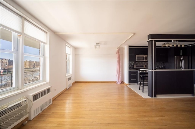 unfurnished living room with radiator, light wood-style floors, and an AC wall unit