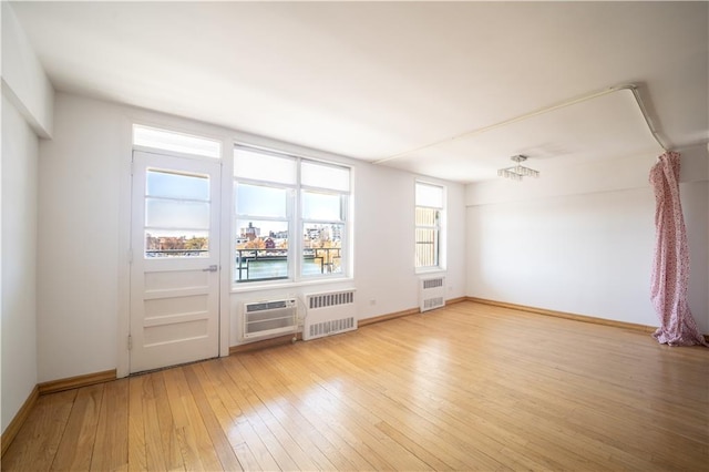 unfurnished room featuring radiator, light wood-style floors, and baseboards