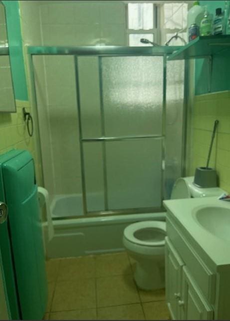 full bathroom featuring tile patterned flooring, shower / bath combination with glass door, vanity, toilet, and tile walls