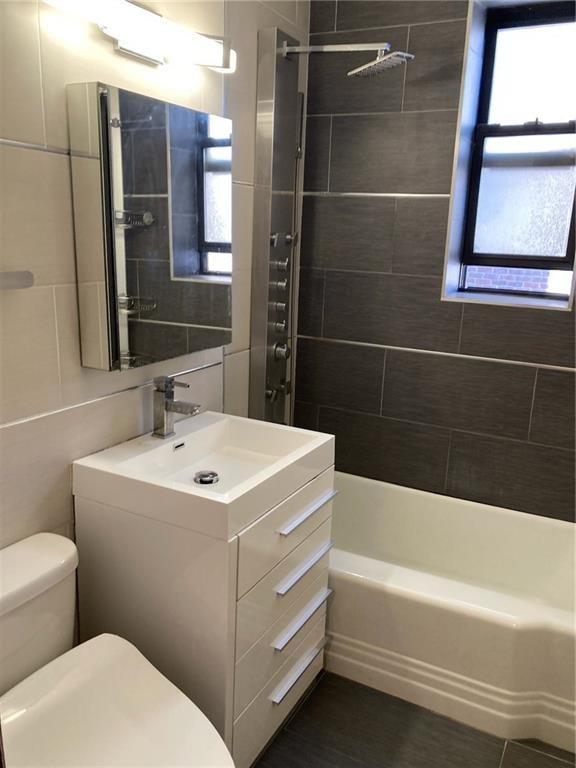 full bathroom with tiled shower / bath, vanity, tile walls, and toilet