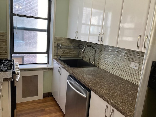 kitchen featuring stainless steel dishwasher, black range oven, sink, dark stone countertops, and white cabinets