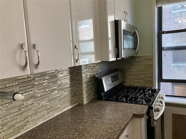 kitchen with white cabinets, stainless steel appliances, tasteful backsplash, and dark stone counters