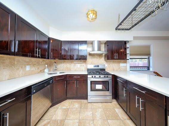 kitchen with wall chimney range hood, sink, stainless steel appliances, tasteful backsplash, and light tile patterned flooring