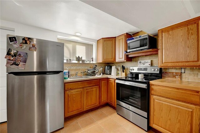 kitchen with sink, backsplash, stainless steel appliances, and light tile patterned flooring