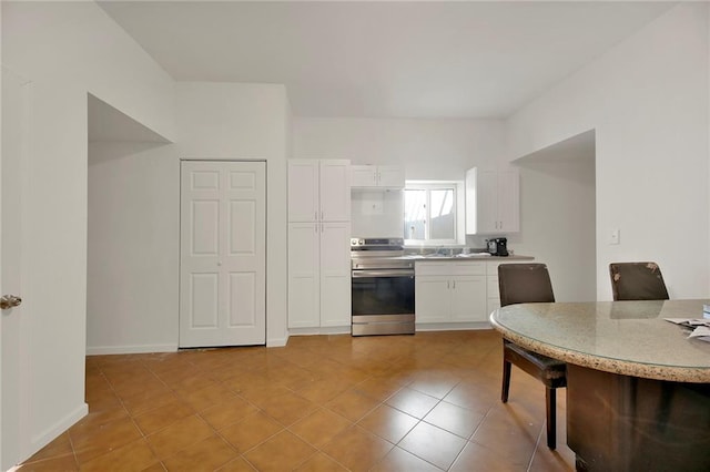 kitchen with light tile patterned floors, stainless steel electric stove, and white cabinets