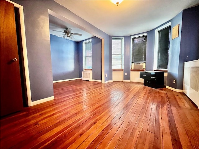 unfurnished bedroom with ceiling fan, cooling unit, wood-type flooring, and radiator heating unit