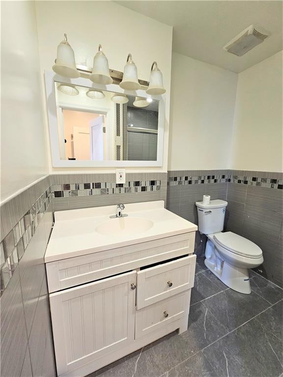 bathroom with toilet, an enclosed shower, vanity, and tile walls