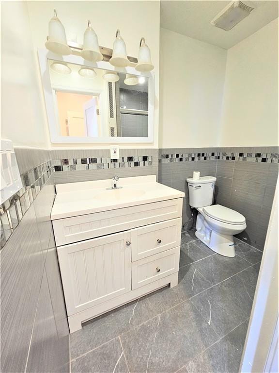 bathroom featuring visible vents, wainscoting, toilet, vanity, and tile walls