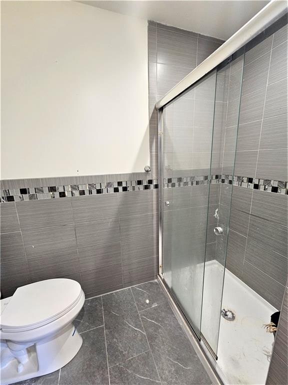 bathroom featuring toilet, marble finish floor, a shower stall, and tile walls