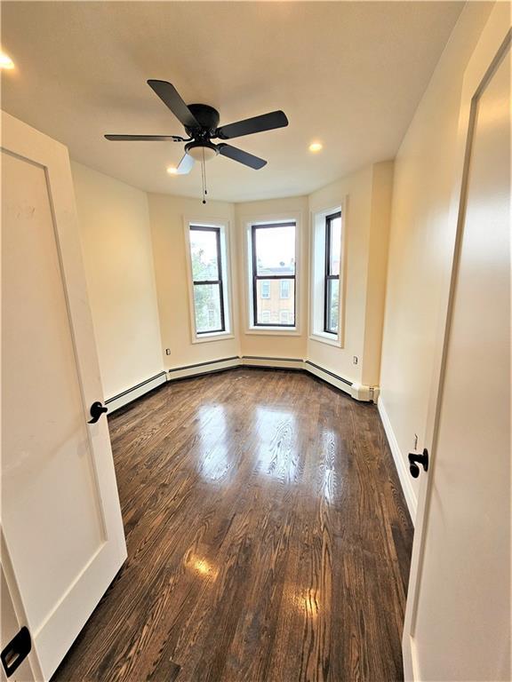 empty room with ceiling fan, dark wood-type flooring, baseboard heating, and baseboards