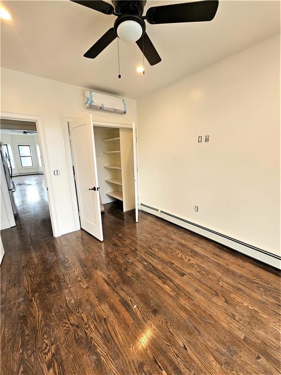 unfurnished bedroom featuring a wall mounted AC, ceiling fan, dark wood-type flooring, refrigerator, and baseboard heating