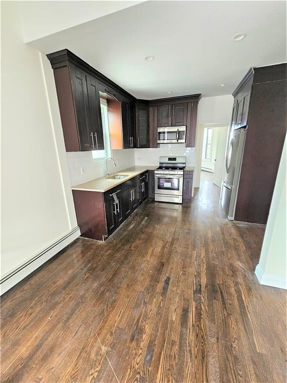 kitchen featuring dark wood-type flooring, a baseboard heating unit, dark brown cabinets, sink, and appliances with stainless steel finishes