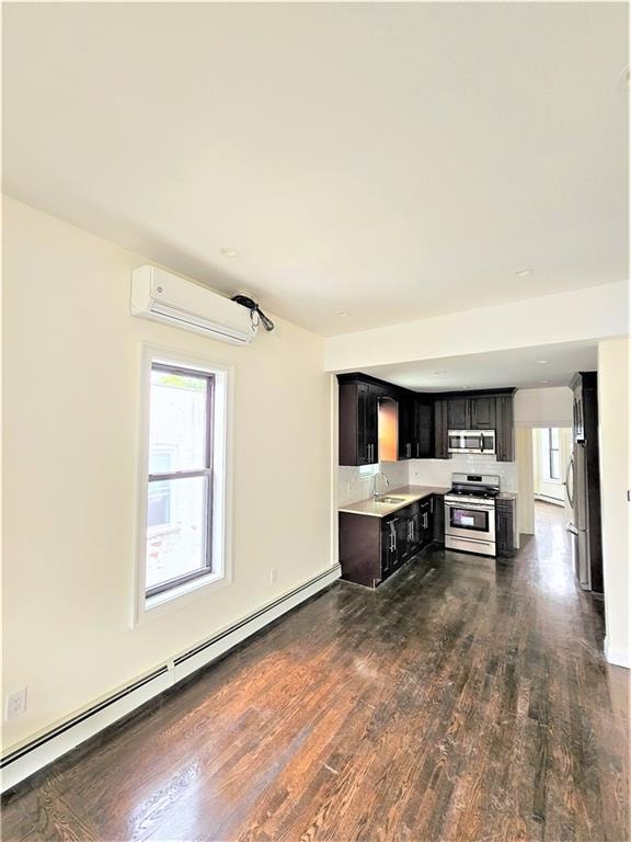 kitchen with dark hardwood / wood-style floors, baseboard heating, a wall mounted air conditioner, stainless steel appliances, and sink