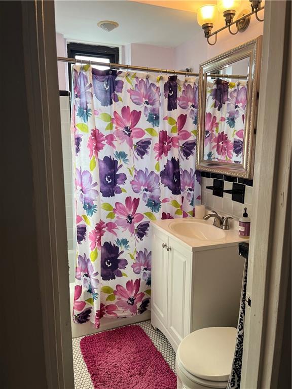 full bathroom featuring toilet, vanity, shower / bath combo with shower curtain, tile patterned flooring, and decorative backsplash