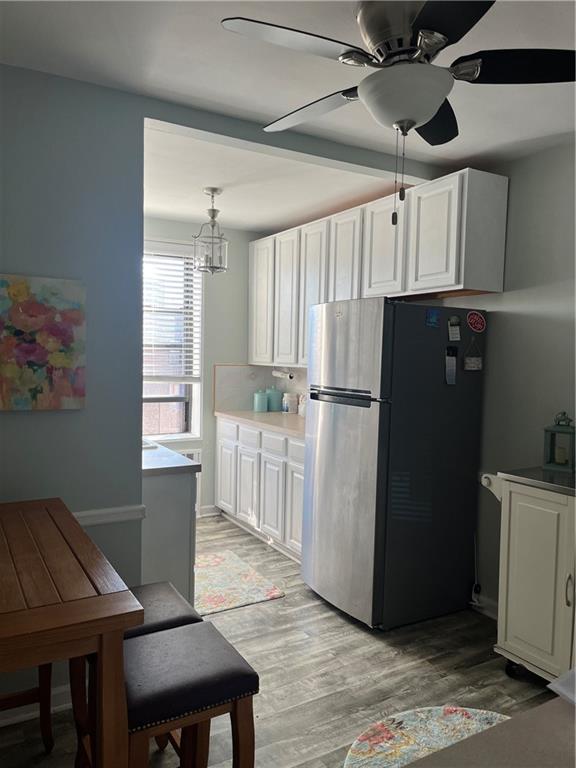 kitchen with pendant lighting, stainless steel fridge, light hardwood / wood-style flooring, white cabinetry, and ceiling fan with notable chandelier