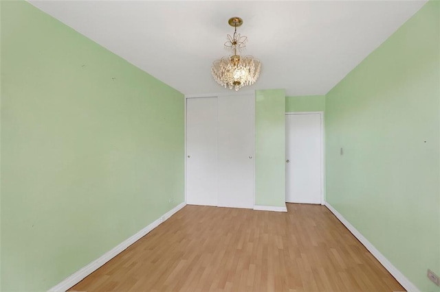 unfurnished room featuring a notable chandelier, baseboards, and wood finished floors