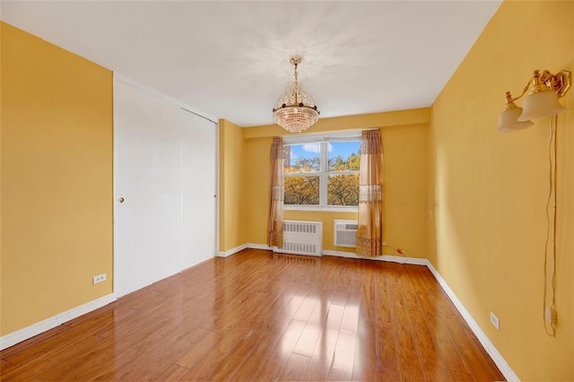 unfurnished room with a chandelier, baseboards, radiator heating unit, and wood finished floors