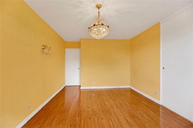 unfurnished room with an inviting chandelier, baseboards, and wood finished floors