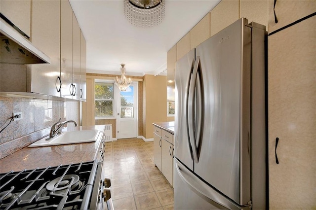 kitchen with under cabinet range hood, a notable chandelier, a sink, freestanding refrigerator, and tasteful backsplash