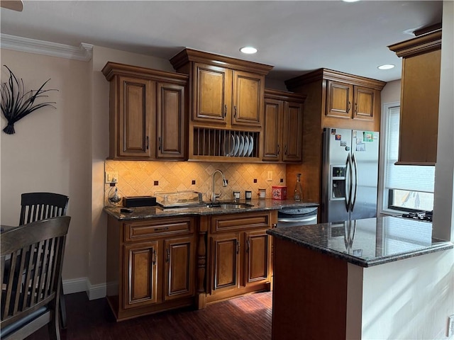 kitchen featuring decorative backsplash, dark wood-style flooring, stainless steel refrigerator with ice dispenser, a sink, and dark stone counters