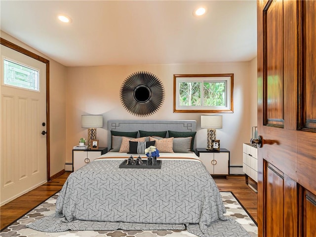 bedroom featuring a baseboard heating unit, dark hardwood / wood-style flooring, and multiple windows