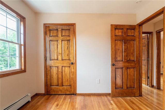 unfurnished bedroom with light hardwood / wood-style flooring, multiple windows, and a baseboard heating unit