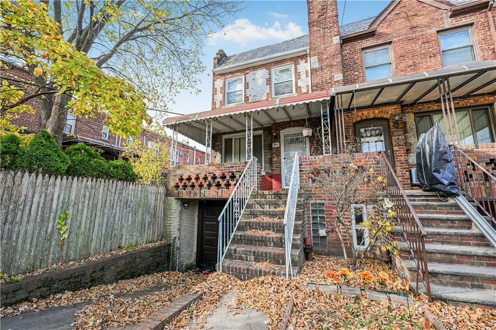 view of front of property featuring stairs, fence, covered porch, and brick siding