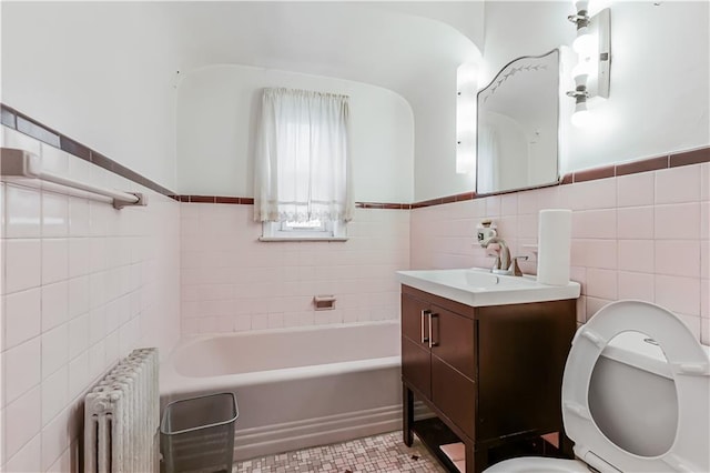 bathroom featuring toilet, tile walls, vanity, radiator, and a bathing tub