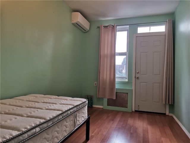 bedroom featuring wood-type flooring, radiator heating unit, and a wall unit AC