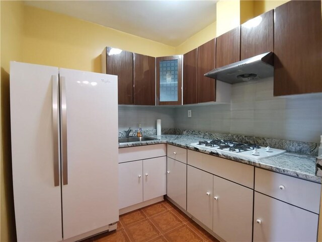 kitchen featuring light stone countertops, tasteful backsplash, white appliances, ventilation hood, and sink