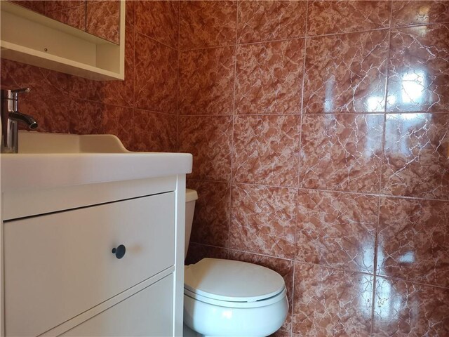 bathroom with vanity, tile walls, and toilet