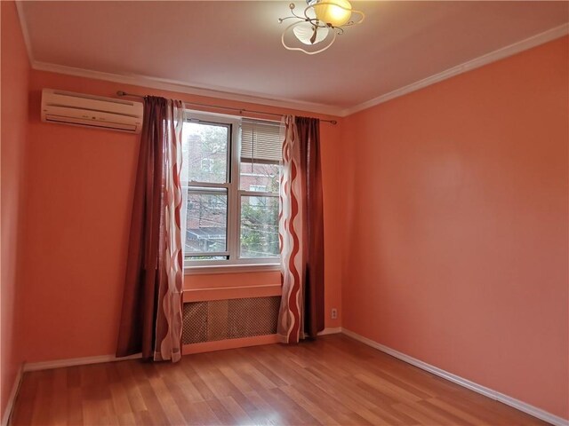 empty room featuring wood-type flooring, an AC wall unit, and ornamental molding