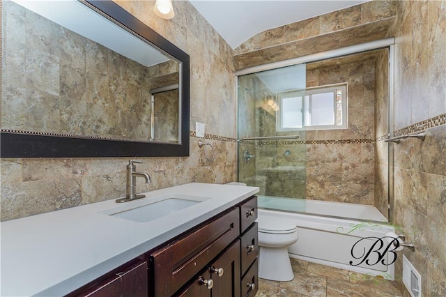 full bath featuring visible vents, bath / shower combo with glass door, toilet, vanity, and tile walls