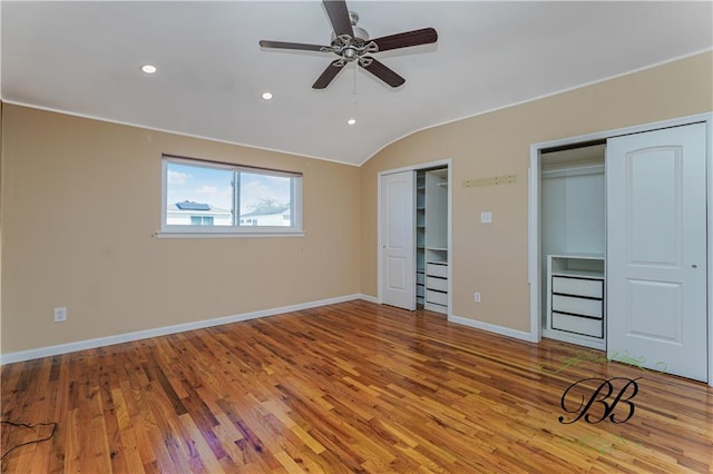 unfurnished bedroom with multiple closets, lofted ceiling, baseboards, and wood finished floors