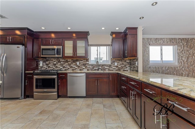 kitchen with appliances with stainless steel finishes, a wealth of natural light, a sink, and light stone counters