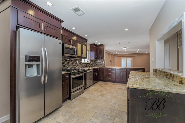 kitchen with stainless steel appliances, a peninsula, a sink, visible vents, and decorative backsplash